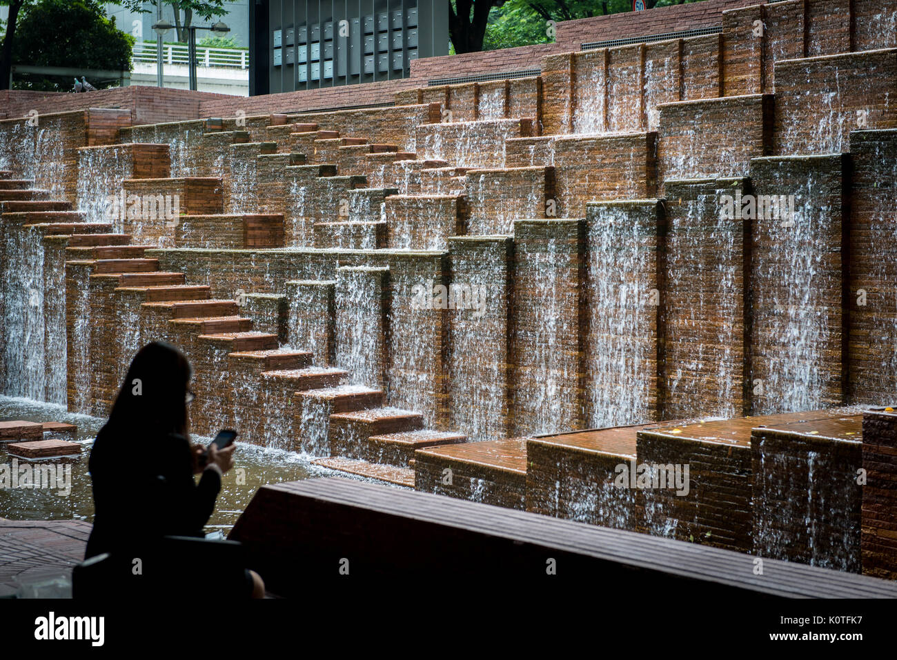 Escalier fontaine d'eau dans un bâtiment de bureau avec femme silhouetée utilisant un appareil mobile Banque D'Images