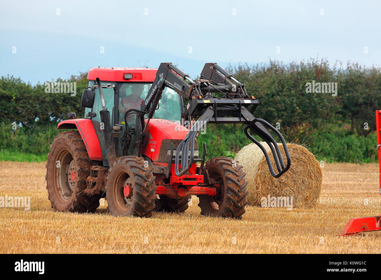 Un agriculteur perçoit sa série de bottes de paille dans un champ avec son  tracteur spécialement adaptés avec une pince pour ramasser les balles  énormes et les faisant tourner Photo Stock -