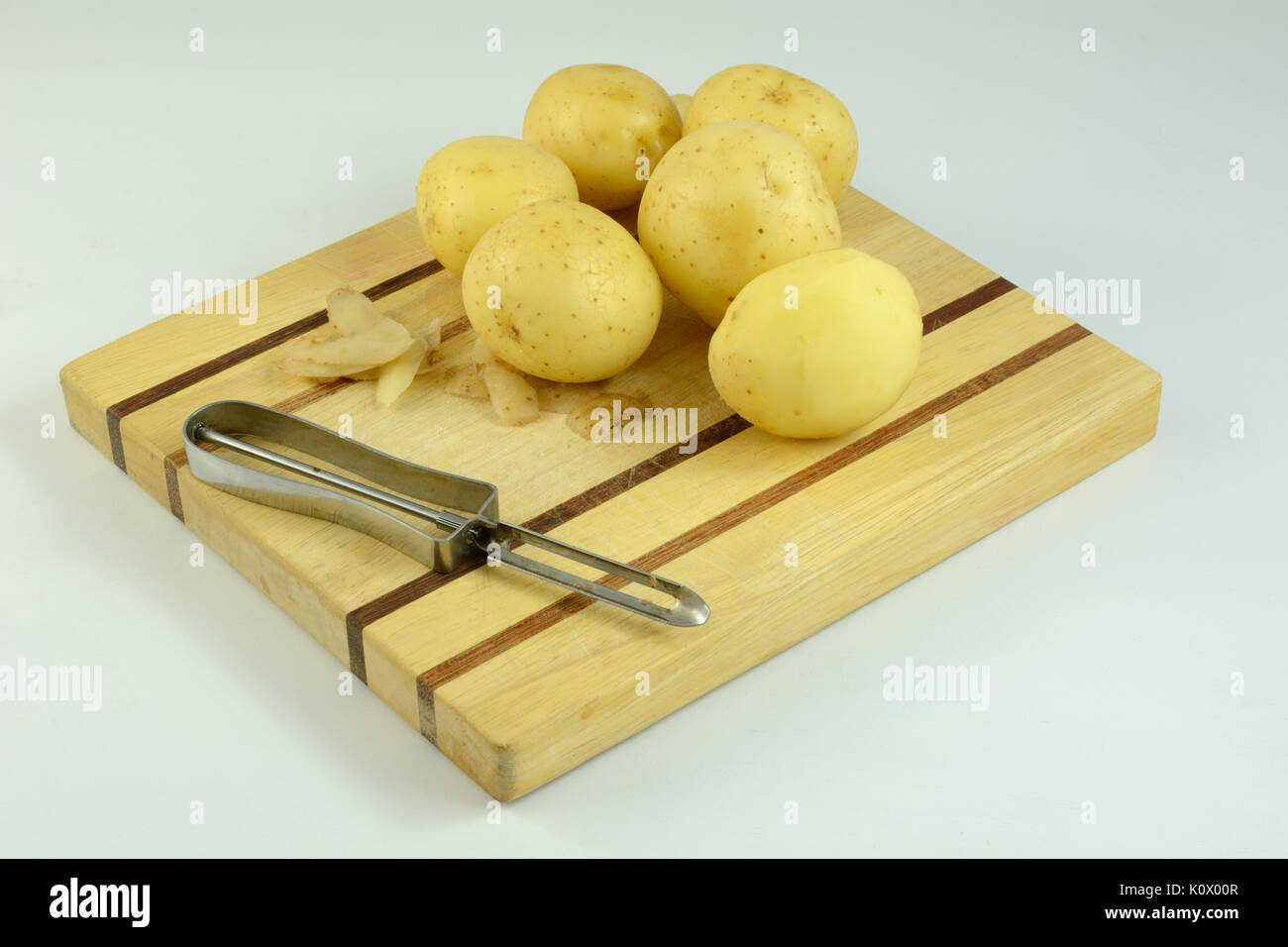 Pelé et pommes de terre non pelées à l'éplucheur sur planche à découper en bois Banque D'Images