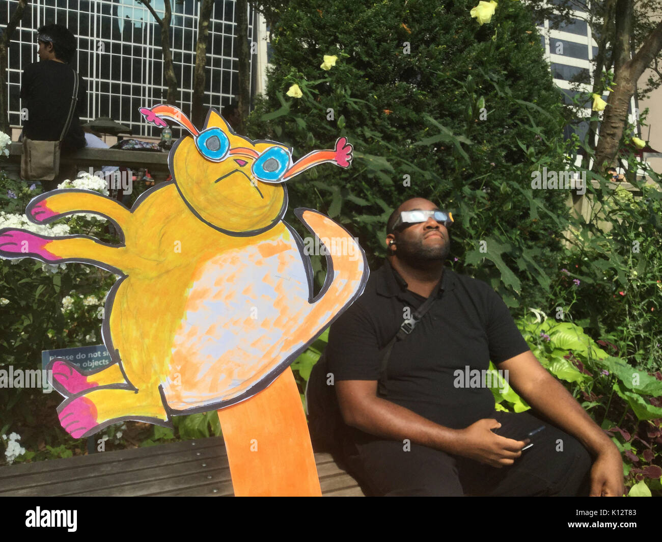 Des milliers de curieux se rassemblent dans Bryant Park pour regarder l'éclipse solaire partielle se produisant à New York Lundi, 21 août, 2017. New York n'est pas dans la bande de totalité avec la lune ne couvrant que presque 72 p. 100 du soleil pendant les 2:44pm maximum. Kat Eclipse, dessiné par Frances M. Roberts se joint à la foule pour regarder l'éclipse. (© Frances M. Roberts) Illustration Banque D'Images
