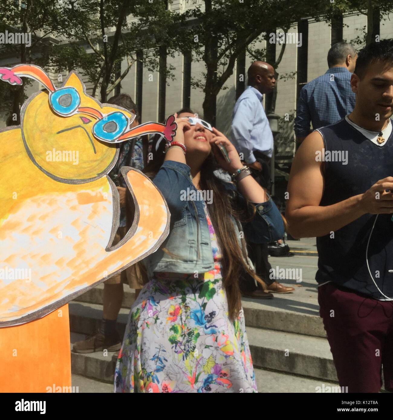 Des milliers de curieux se rassemblent dans Bryant Park pour regarder l'éclipse solaire partielle se produisant à New York Lundi, 21 août, 2017. New York n'est pas dans la bande de totalité avec la lune ne couvrant que presque 72 p. 100 du soleil pendant les 2:44pm maximum. Kat Eclipse, dessiné par Frances M. Roberts se joint à la foule pour regarder l'éclipse. (© Frances M. Roberts) Illustration Banque D'Images