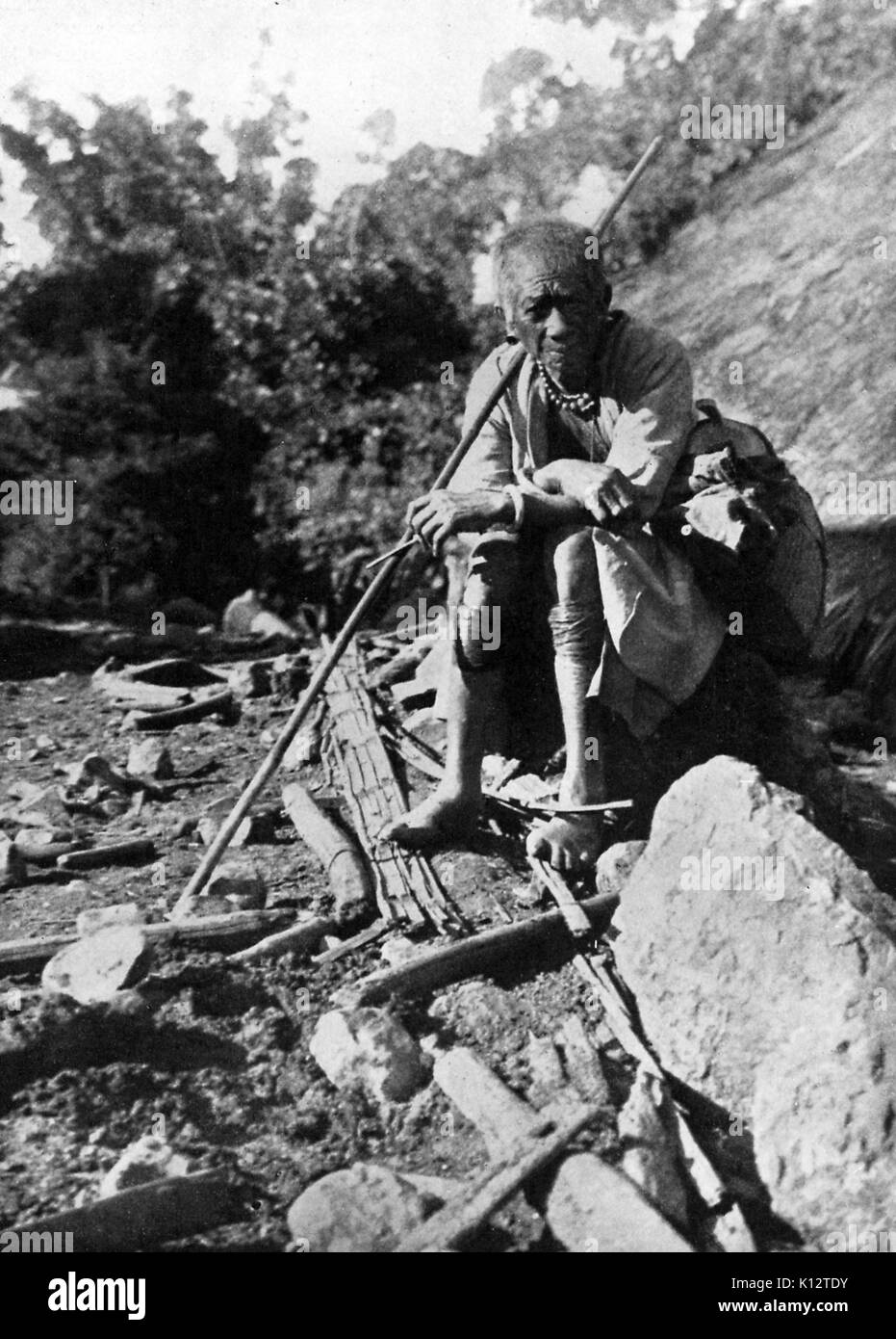 Baccalauréat en Guangto assis sur un rocher et tenant un poteau en bois, 1922. Banque D'Images