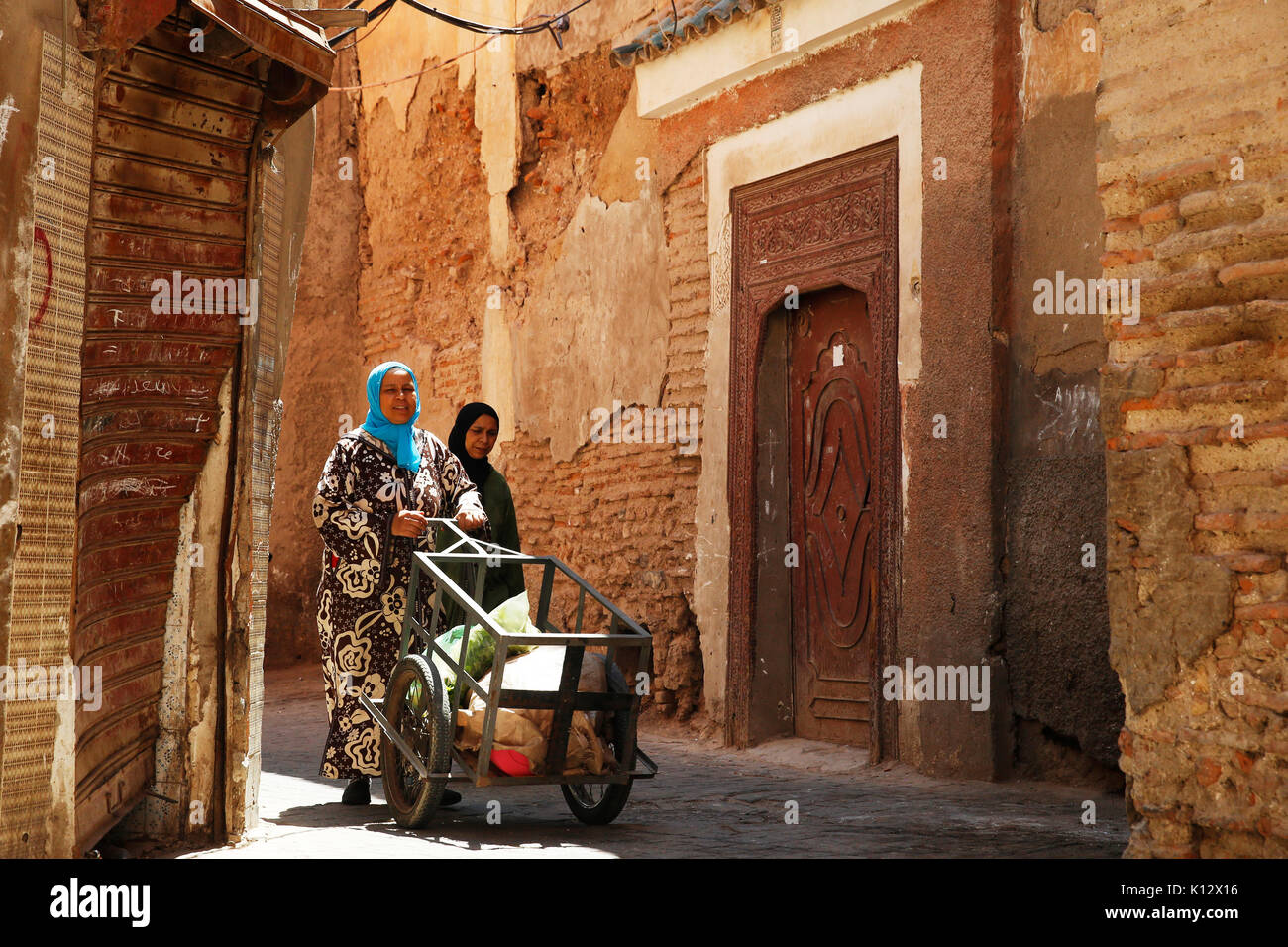 Les femmes avec couvre-chef pousser un panier à travers les rues étroites médina avec des murs orange à Marrkech au Maroc Photographie : © Luke MacGregor  +44 (0) 79 Banque D'Images