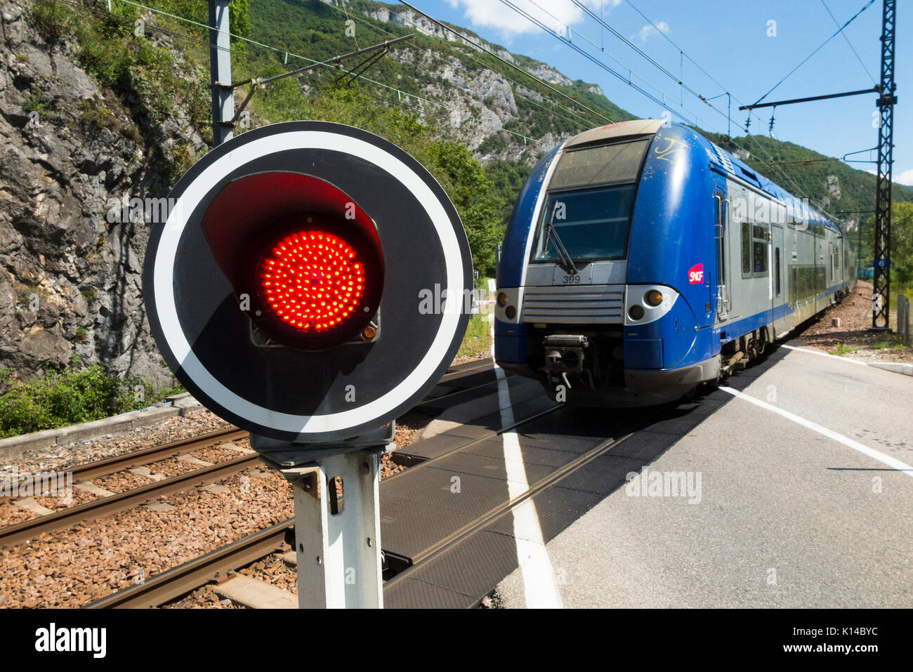 Passage rapide en train et un signal rouge indique / feux clignotants / feux d'avertissement pour les voitures à un passage à niveau automatique de chemin de fer français en France. Banque D'Images