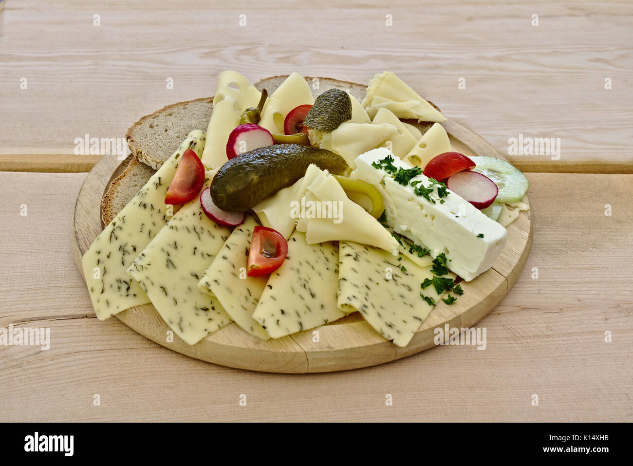 Divers fromages disposées sur une plaque en bois avec des tomates, des cornichons et de la lame. Banque D'Images