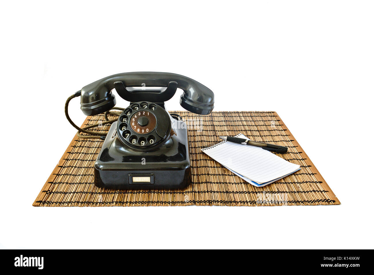Téléphone vintage sur tapis en rotin avec stylo noir et bloc-notes avec copyspace isolé sur fond blanc Banque D'Images