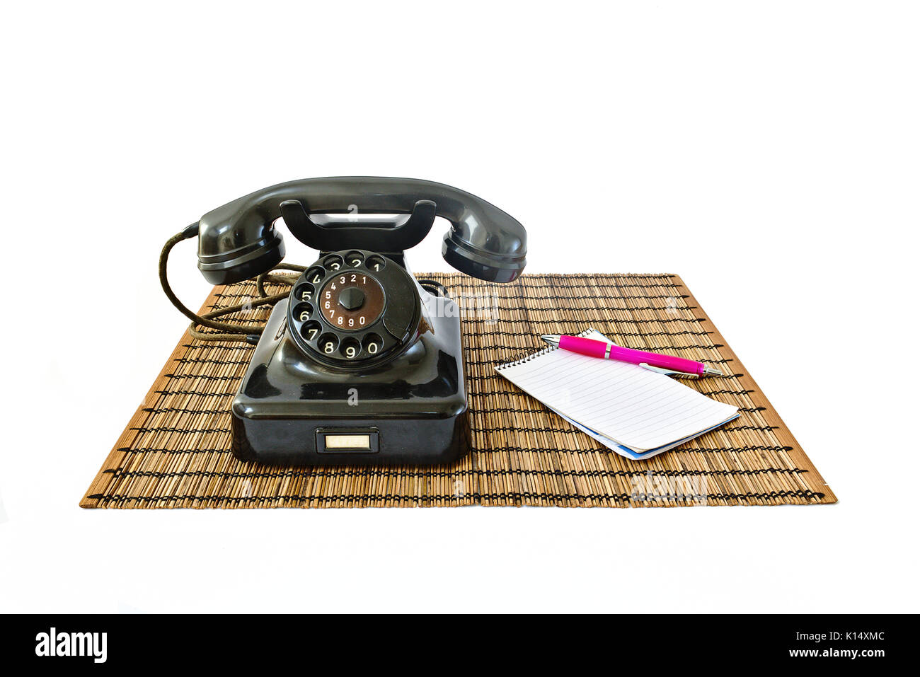 Téléphone vintage sur tapis en rotin avec bloc-notes et stylo rose avec copyspace isolé sur fond blanc Banque D'Images