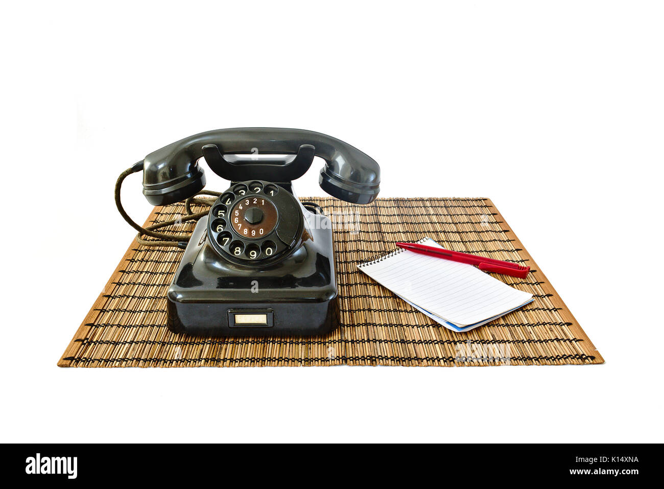 Téléphone vintage sur tapis en rotin avec stylo rouge et le bloc-notes avec copyspace isolé sur fond blanc Banque D'Images