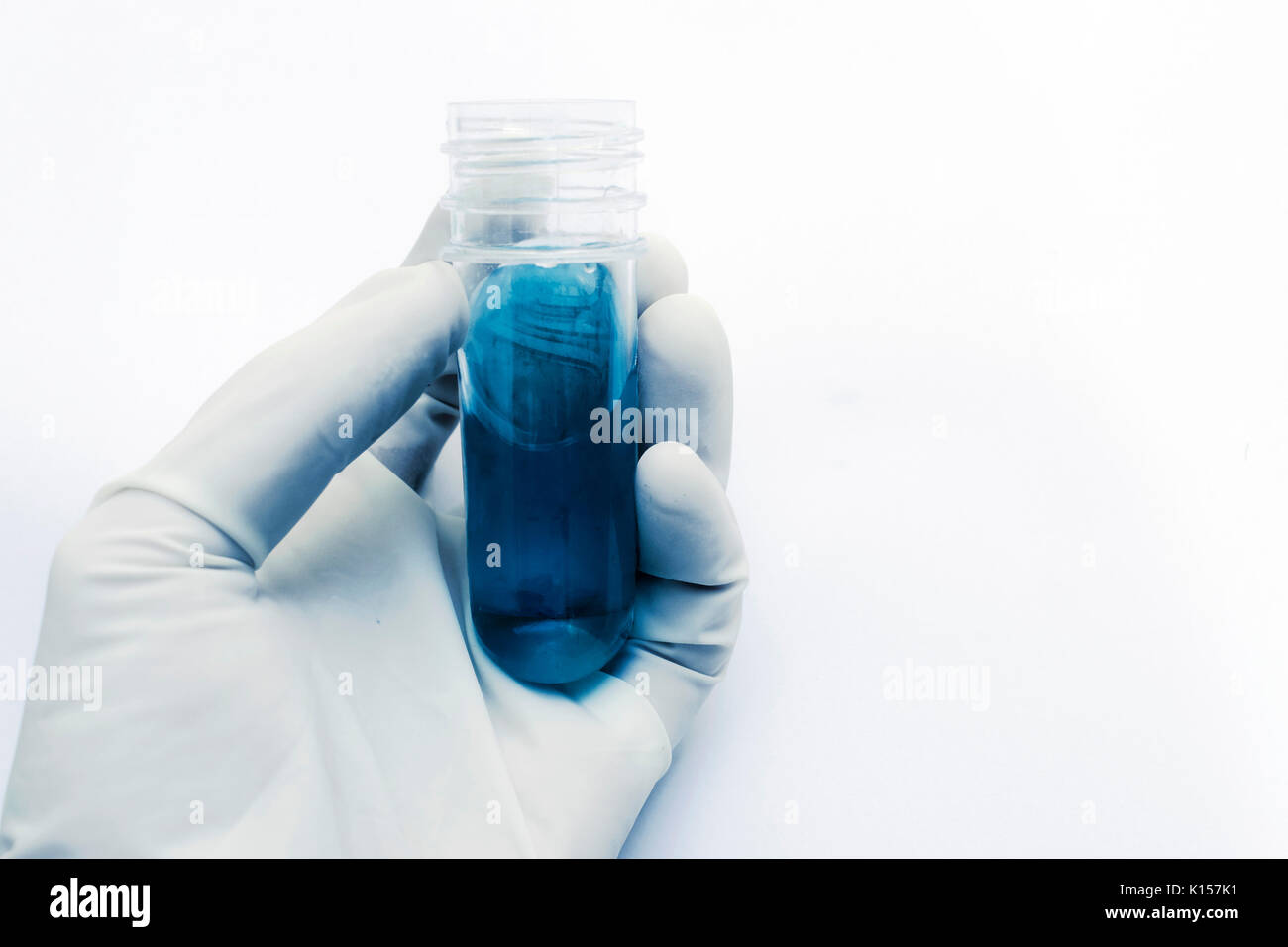 La main avec des gants en latex tenant un verre de laboratoire de test tube de liquide bleu et des tons bleus, sur fond blanc Banque D'Images