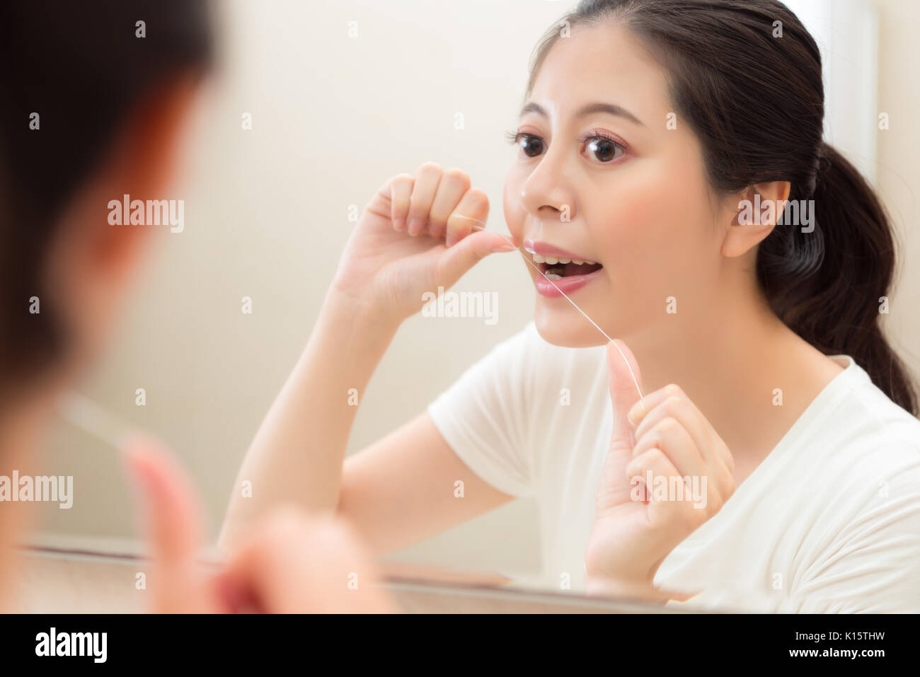 Photo gros plan de fille élégante attrayante en utilisant la soie dentaire dents propre écart éviter nourriture restante sur les dents à l'image de réflexion miroir dans la salle de bains. Banque D'Images