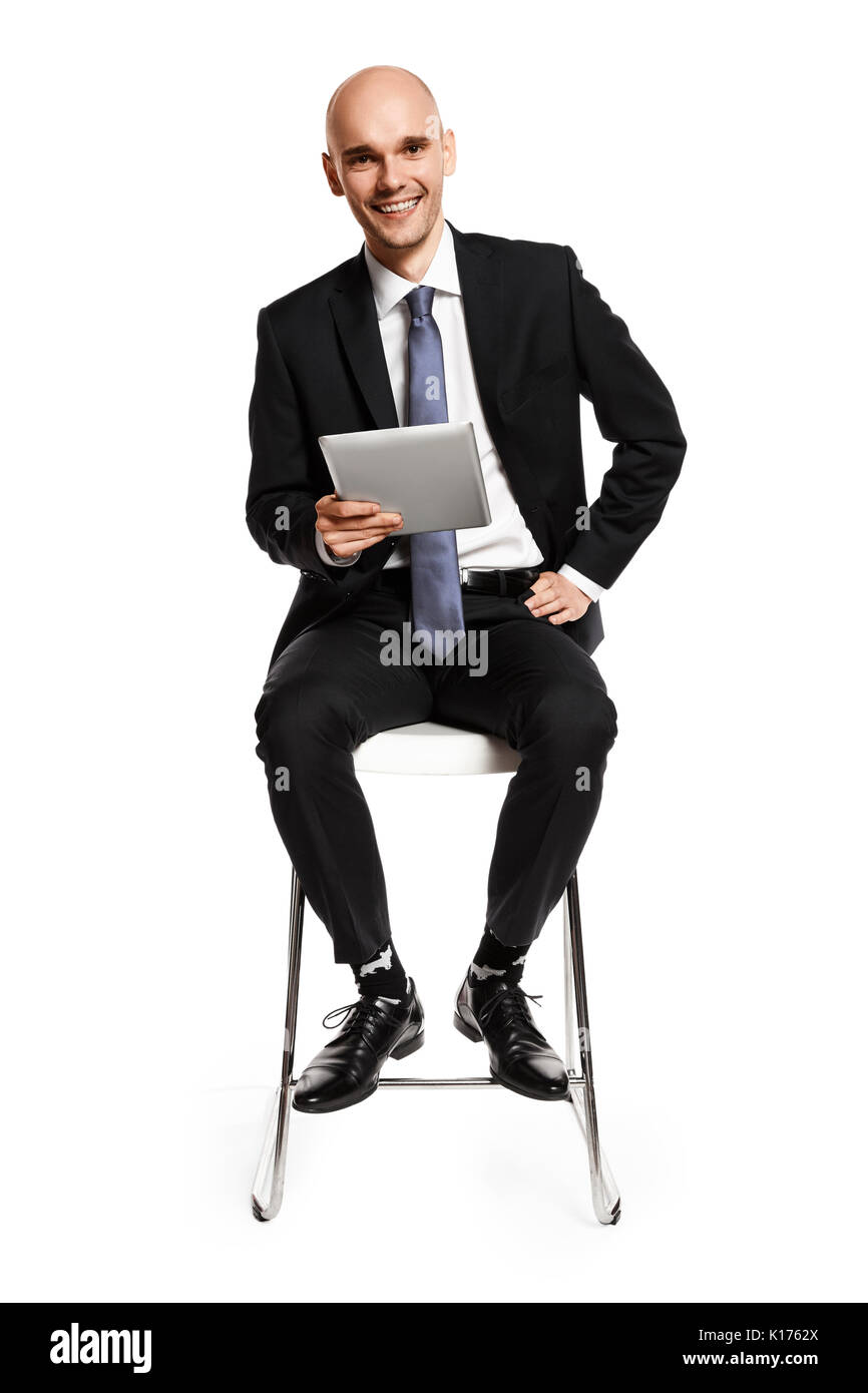 Cheerful young businessman assis sur une chaise avec une tablette numérique. Isolé sur fond blanc. Banque D'Images