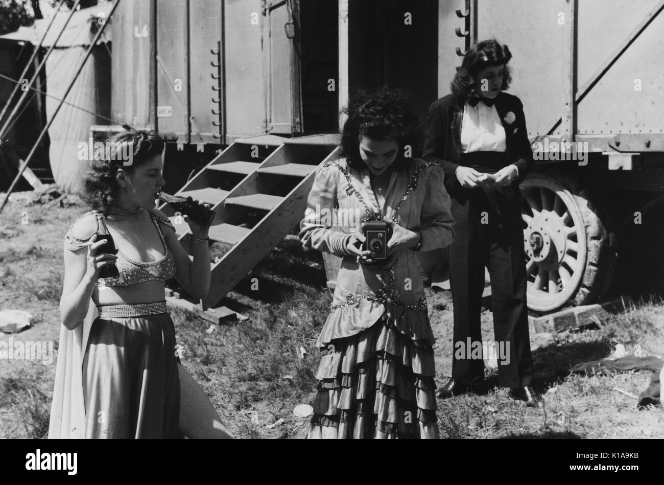 Deux femmes artistes, l'un habillé en danseuse du ventre, l'autre habillé en magicien, tandis qu'une troisième femme prend une photo, devant un wagon qui a été placé sur les roues et transportés vers le parc des expositions dans le cadre d'un spectacle girlie, Rutland, Vermont, 1941. À partir de la Bibliothèque publique de New York. Banque D'Images