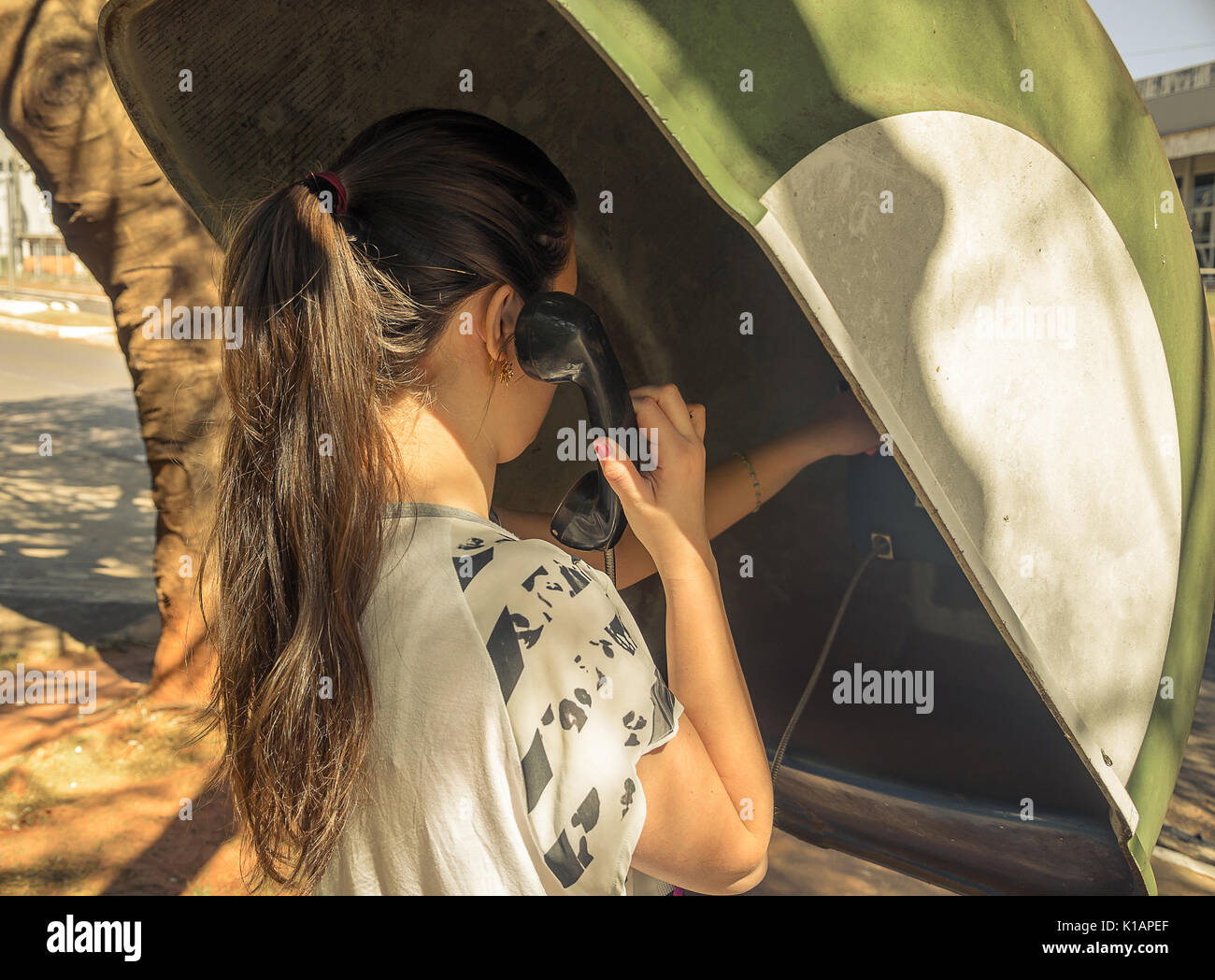 Girl, de tenir le téléphone, sur son dos, à parler au téléphone public. Banque D'Images