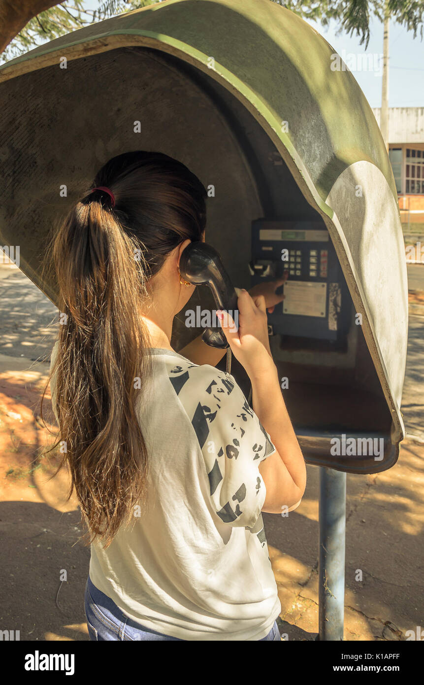 Girl, de tenir le téléphone, sur son dos, à parler au téléphone public. Banque D'Images