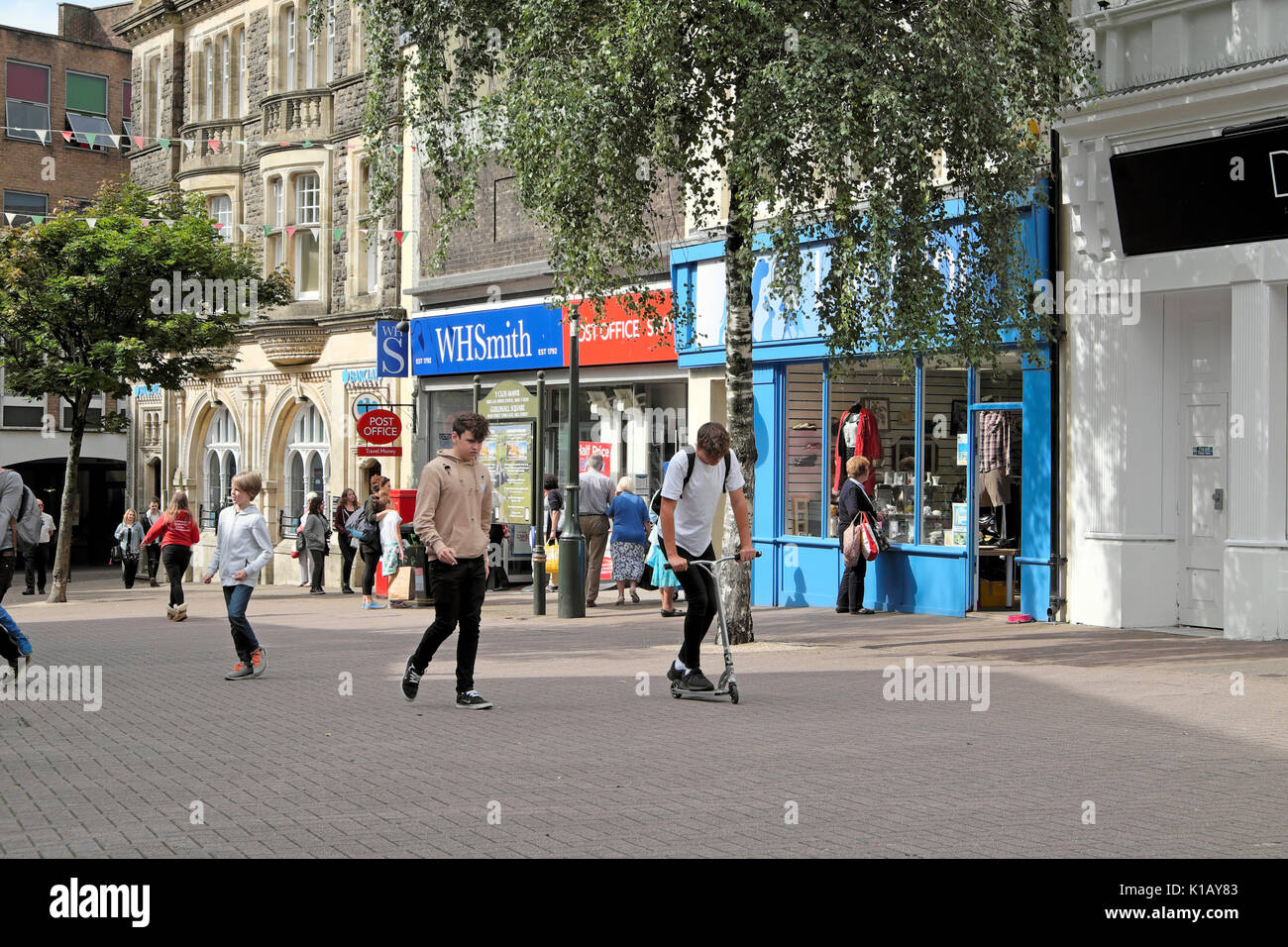 Teen boy with scooter marcher avec ami près de boutiques dans Guildhall Square passé WH Smith store summer Carmarthenshire Carmarthen Wales UK KATHY DEWITT Banque D'Images