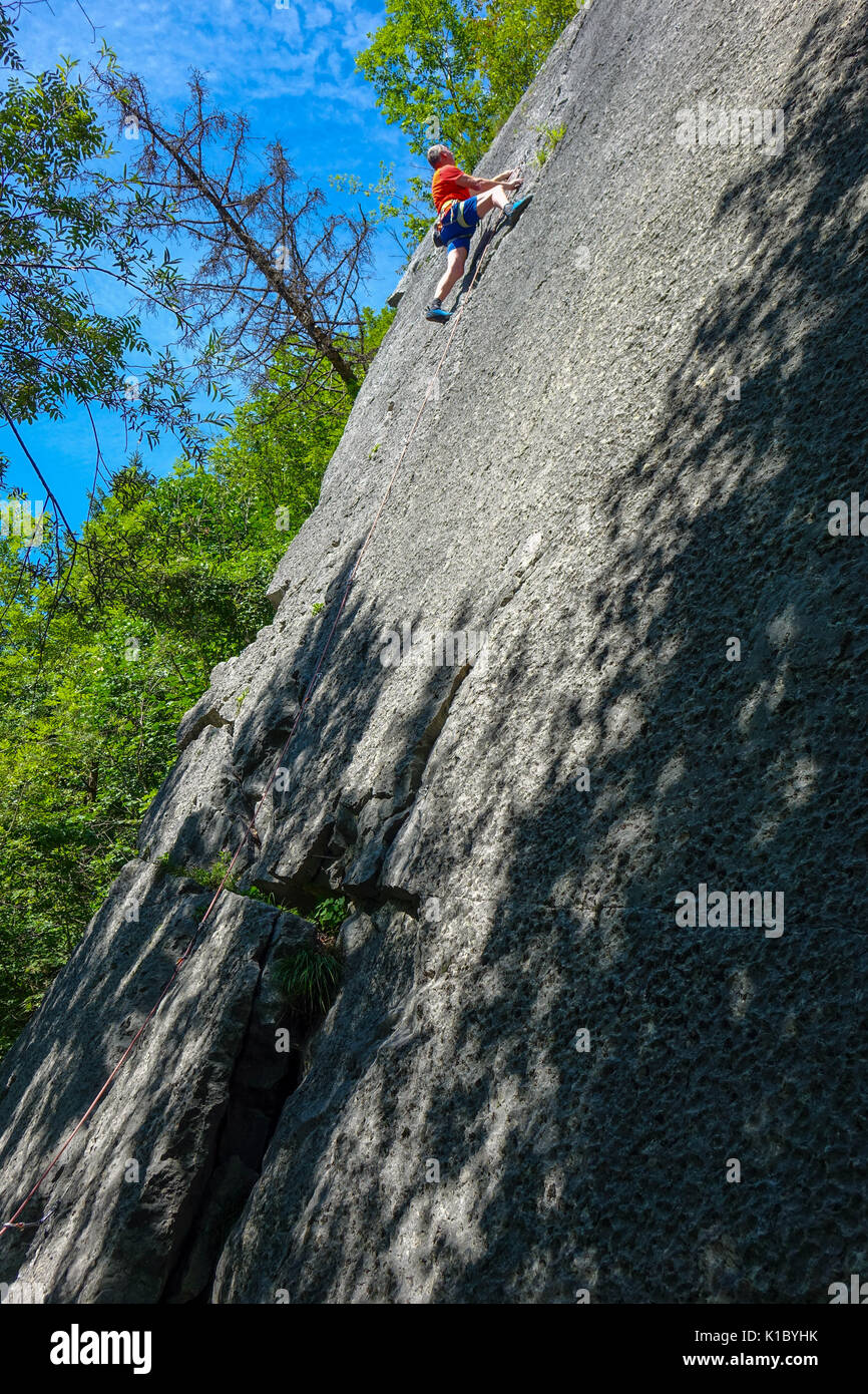 Male rock climber expérimentés en rouge sur le rocher lisse face, près de Reutte, Austris Banque D'Images