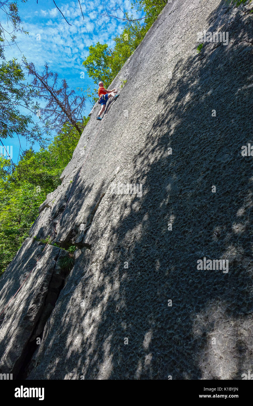 Male rock climber expérimentés en rouge sur le rocher lisse face, près de Reutte, Austris Banque D'Images