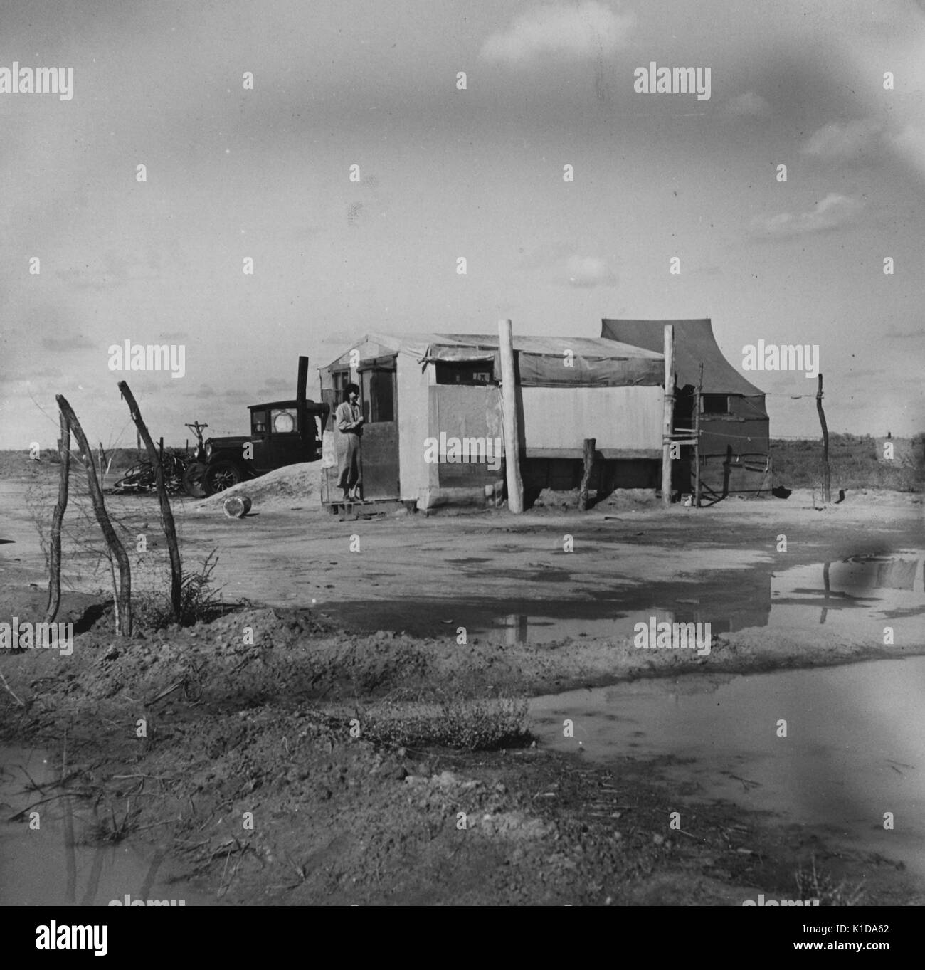L'homme entre dans une grande tente dans un camp de migration avec divers bâtiments et une corde à linge, entouré de flaques d'eau, en Californie, 1936. à partir de la bibliothèque publique de new york. Banque D'Images