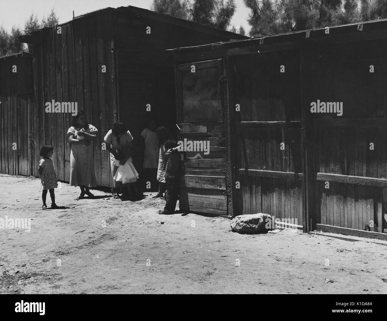 La famille mexicaine, avec des femmes et des filles, debout sur un chemin de terre, entre deux bâtiments de ferme en bois, Californie, 1935. à partir de la bibliothèque publique de new york. Banque D'Images