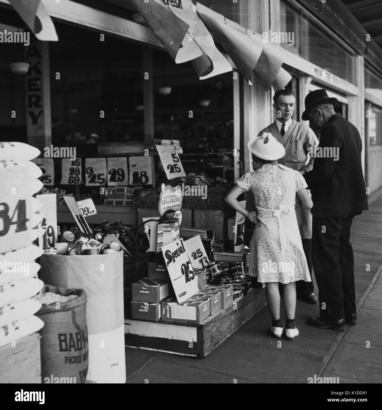Couple effectuant des achats auprès d'un fournisseur dans une boutique du marché, Portland, Oregon, 1936. De la bibliothèque publique de New York. Banque D'Images
