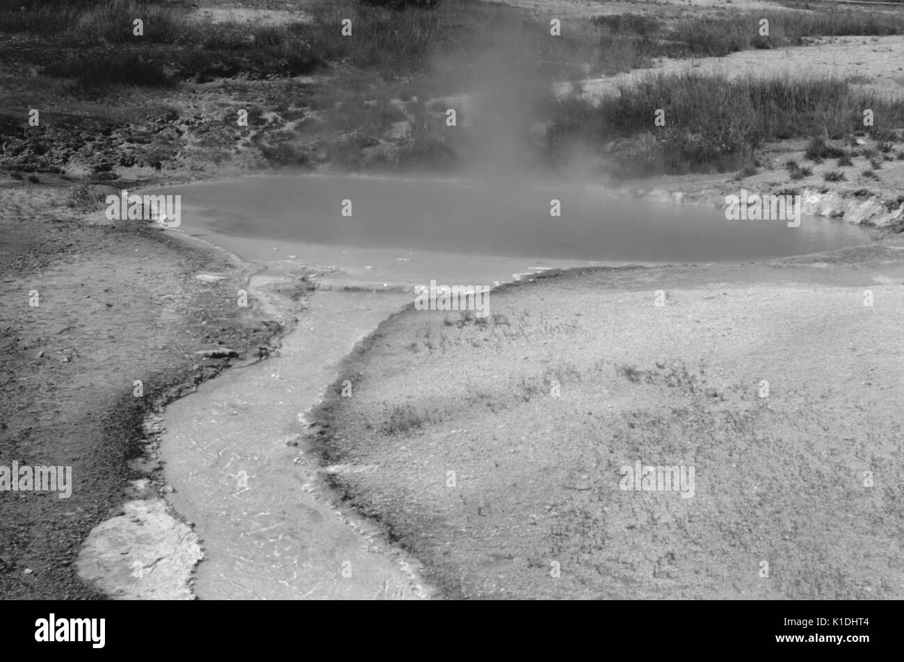 Un printemps chaud, composé d'eau bleue qui donne la pression et un flux d'argile gris, rempli de l'eau s'écoule hors de la source d'eau chaude, sol entourant la source d'eau chaude est soit stérile ou contient de très petites de la végétation, le Parc National de Yellowstone, Wyoming, 1975. Banque D'Images