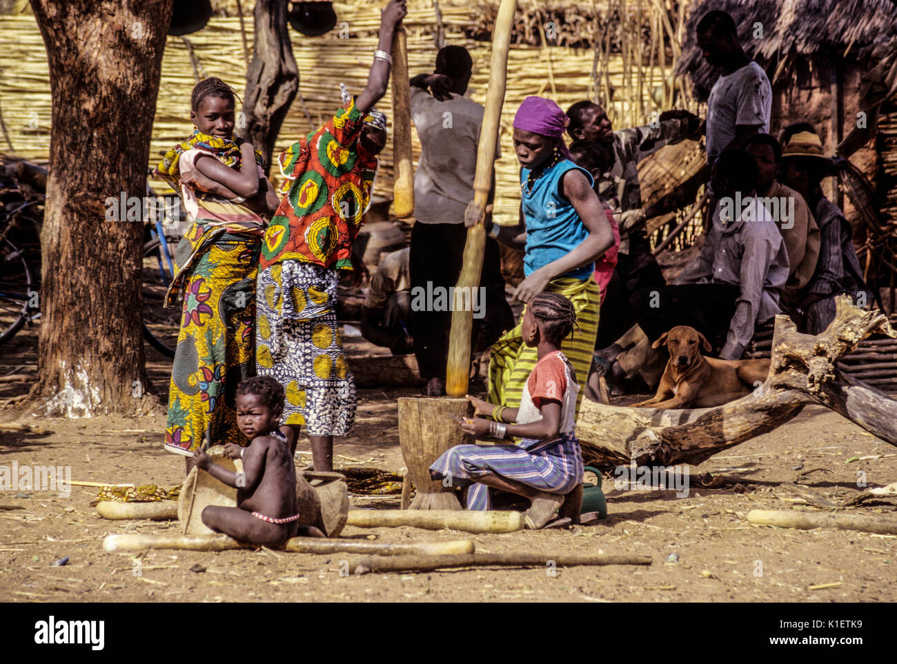 Djiliki, au Niger. Les hommes parlent de village en arrière-plan tandis que les femmes travaillent, battre le mil pour faire de la farine. Banque D'Images