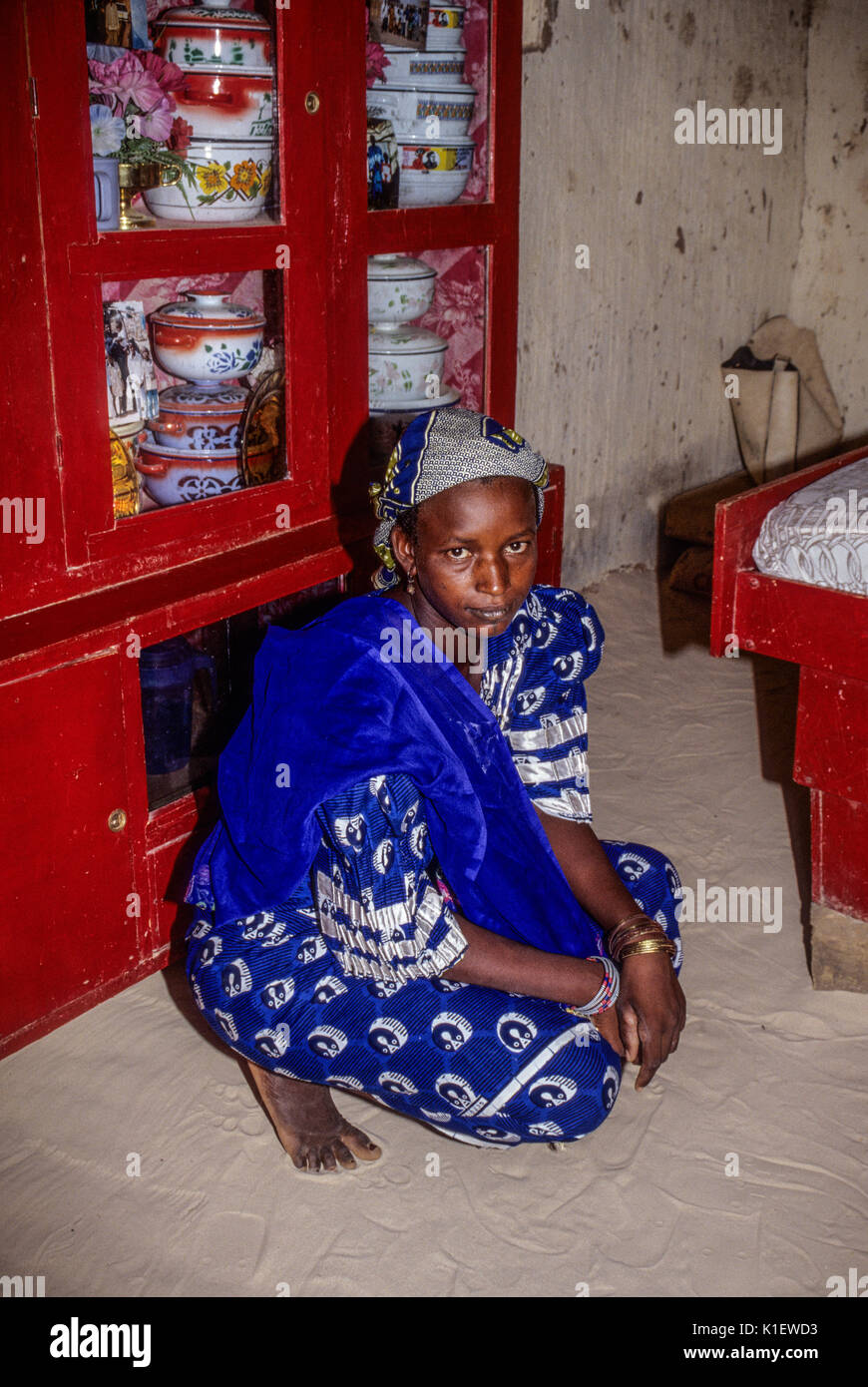 Le Niger, Afrique de l'Ouest. Femme peule dans sa maison. Ustensiles de service en armoire, du sable sur le sol. Banque D'Images