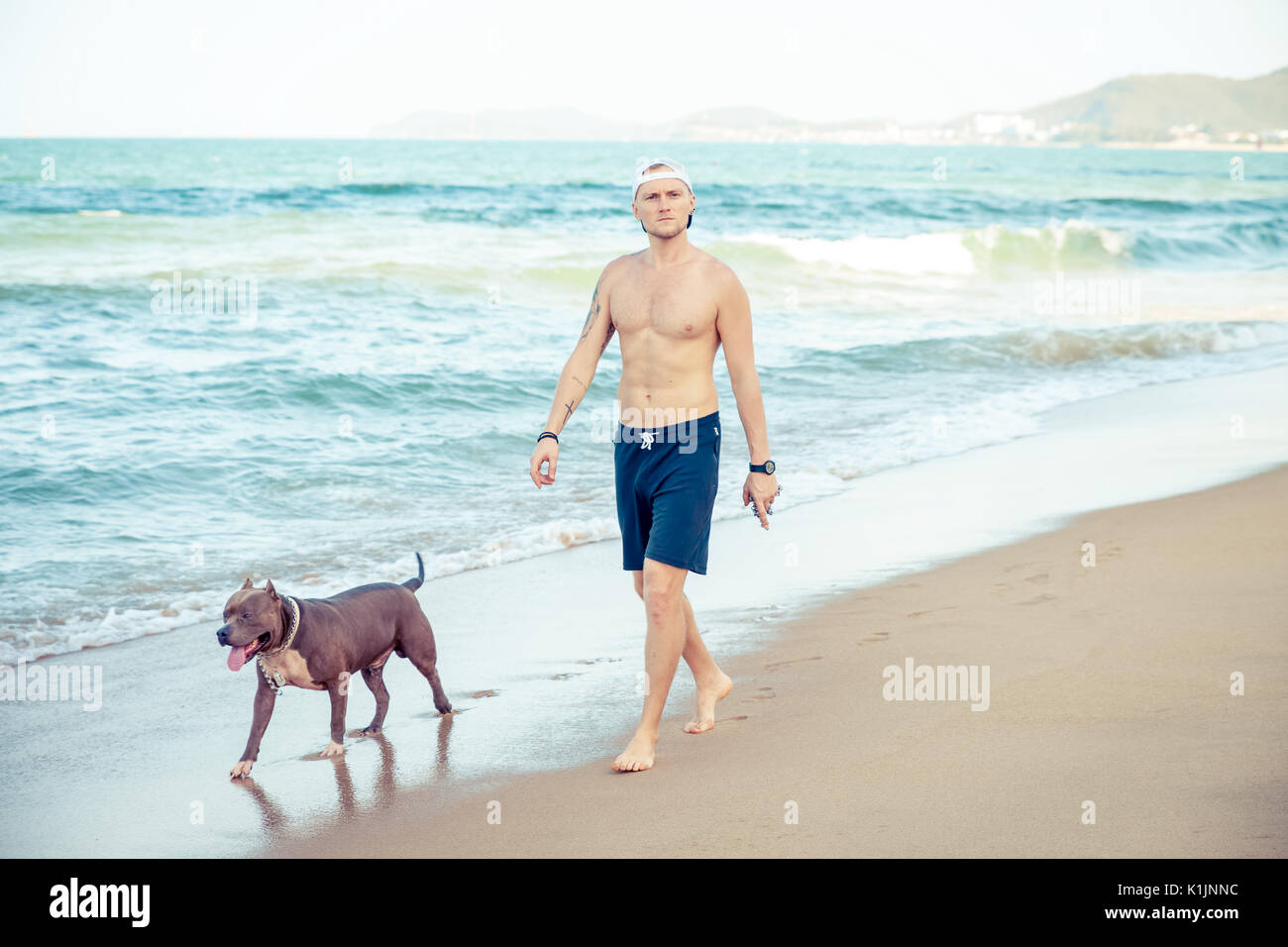 Jeune homme avec chien bull-terrier américain de mine marche sur mer Banque D'Images