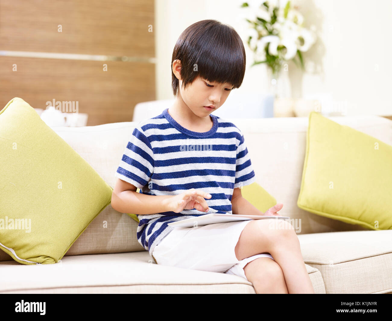 Enfant asiatique assis seul sur le jeu de table with digital tablet Banque D'Images