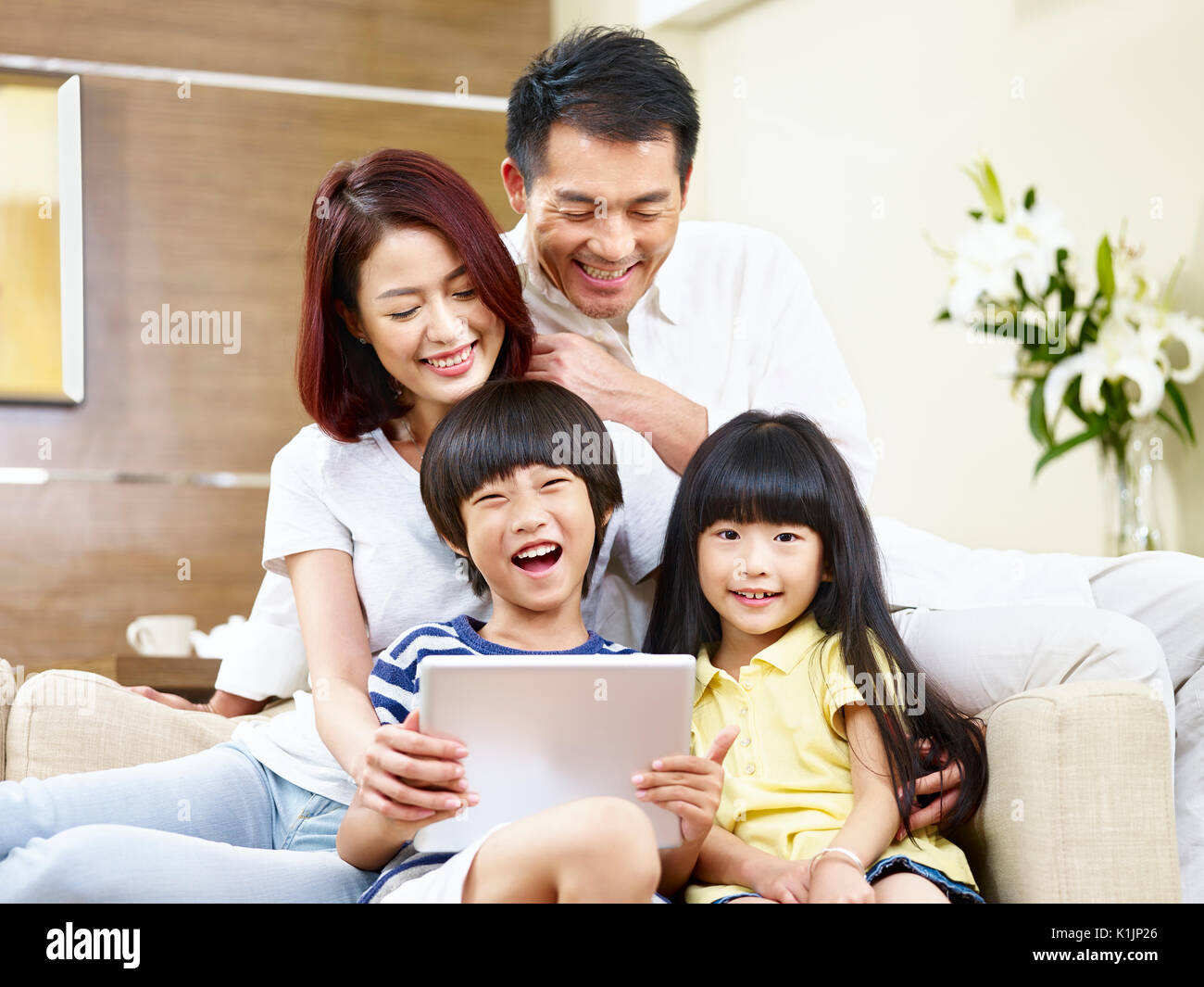 Les parents asiatiques et les enfants sitting on couch having fun with digital tablet. Banque D'Images