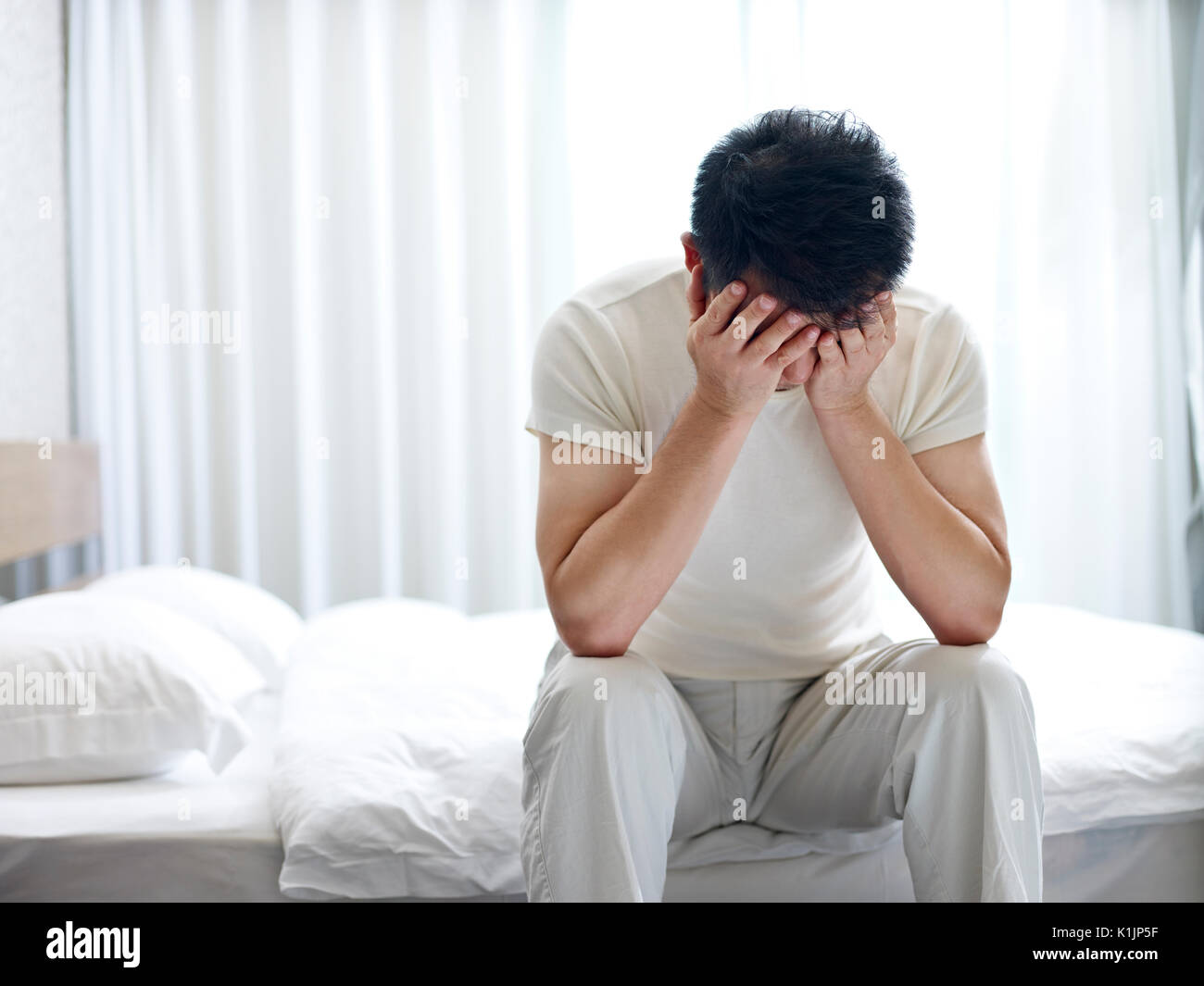 Asian homme souffrant d'insomnie assis sur le lit la tête en bas, couvrant le visage avec les mains. Banque D'Images