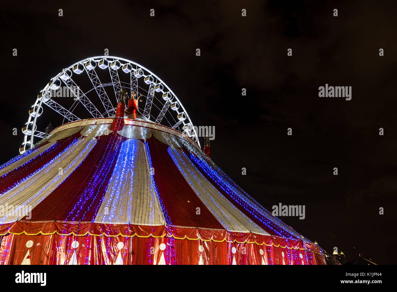 Grande roue illuminée et un chapiteau rouge et blanc tente de cirque tourné de nuit. Banque D'Images