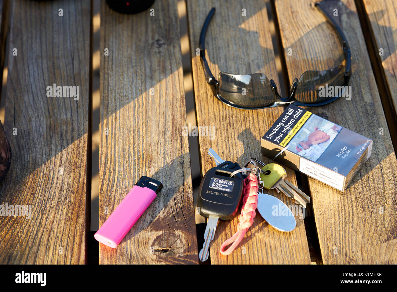 Des clés de voiture, Fag packet,lunettes Oakley et d'un briquet rose sur une table en bois Banque D'Images