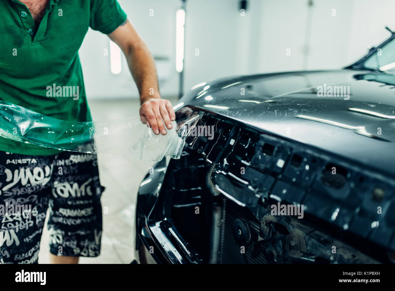 L'homme installe un film de protection peinture automobile sur le capot. Revêtement de protection transparent contre les éclats et égratignures Banque D'Images