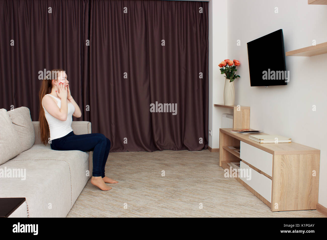 Peur jeune femme regardant la télévision. Brunette girl sitting on couch avec un oreiller près de la face Banque D'Images