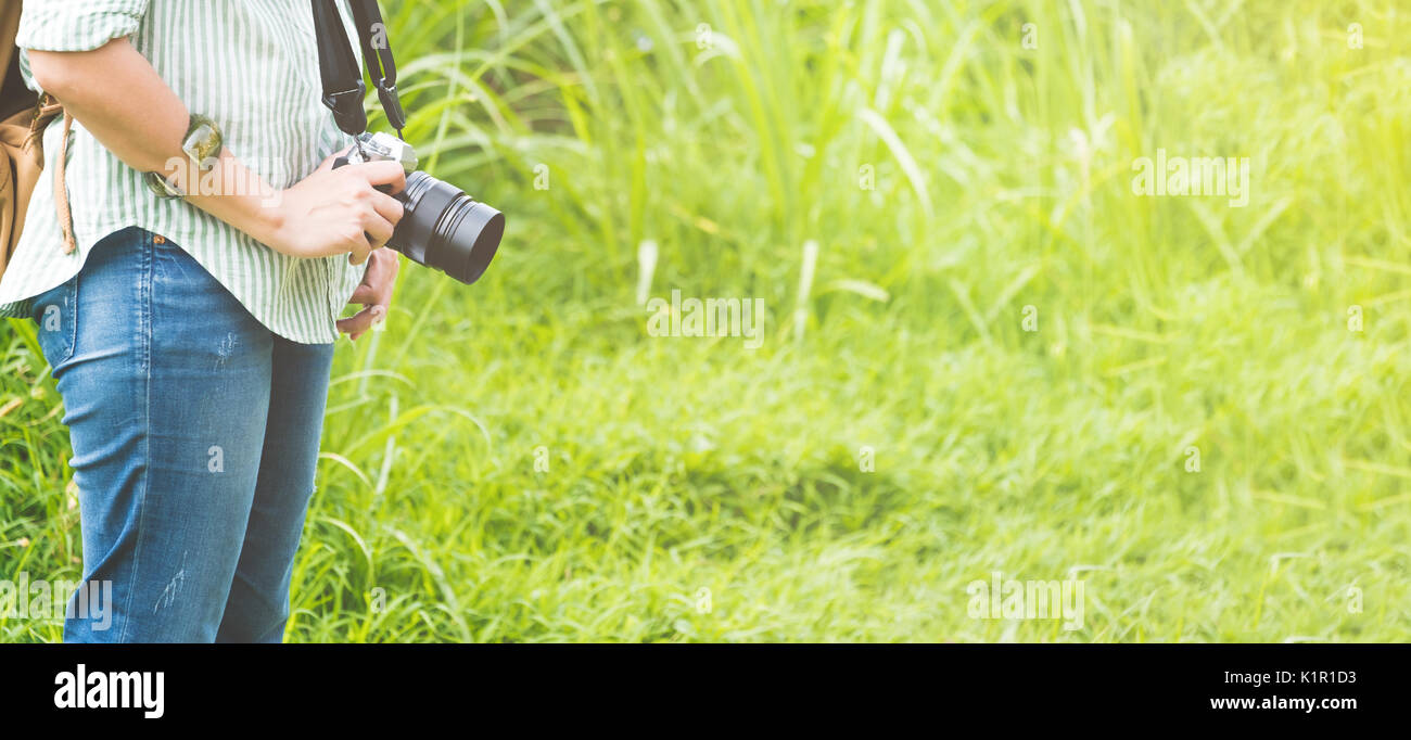 Woman backpacker traveler holding camera debout dans l'herbe verte de patch en matin,Travel,concept wanderlust taille bannière laisser un espace pour l'ajout de texte Banque D'Images