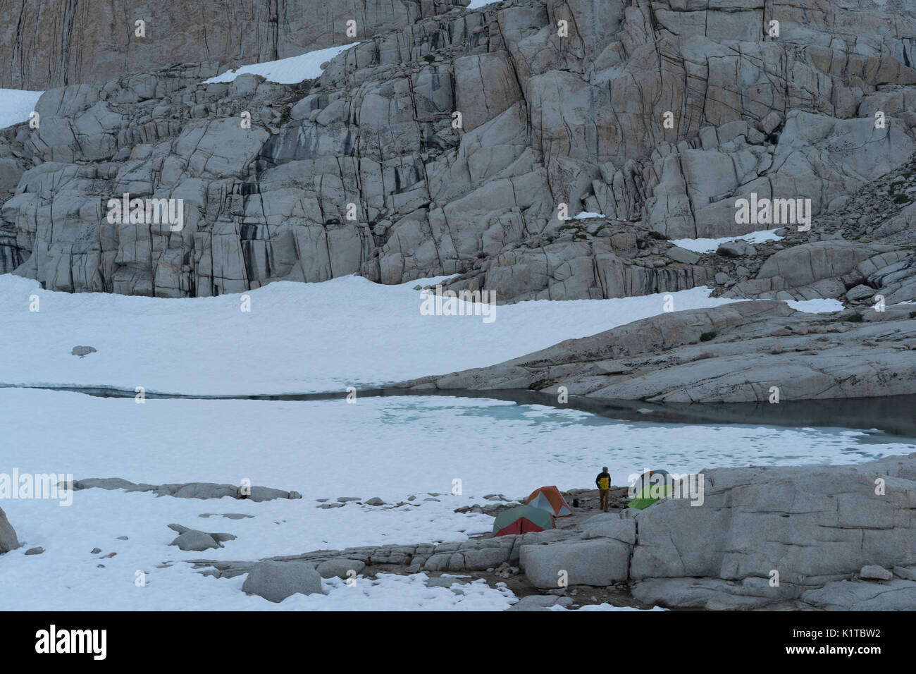 Un randonneur fait une pause entre les tentes au camp Trail sur le Mt. Whitney Trail, à côté de la neige et un lac gelé. Banque D'Images