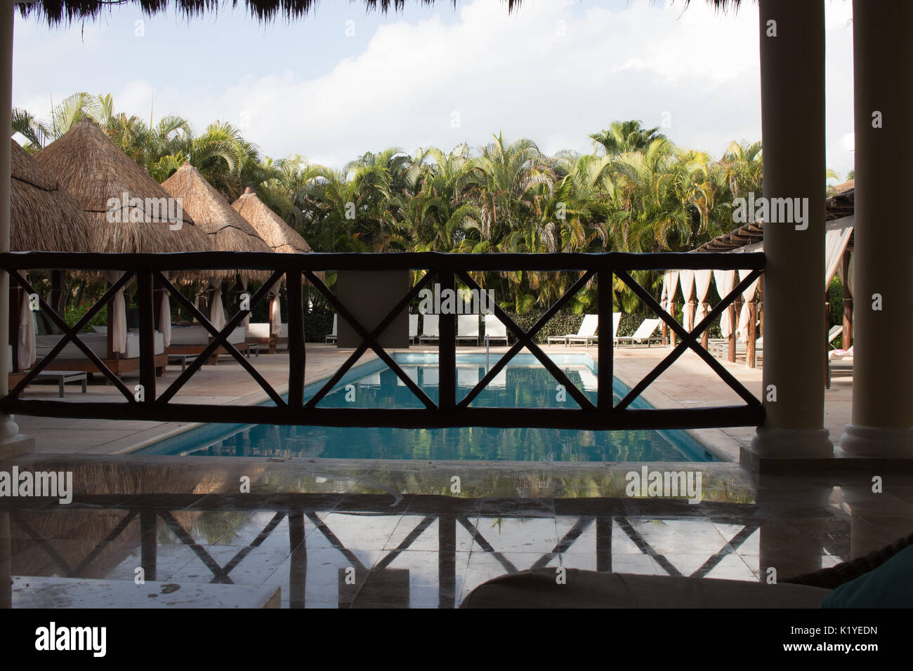 Piscine claire vu de l'ombre à une cabane de patio en marbre et cabanas autour de piscine et palmiers dans la distance. Banque D'Images