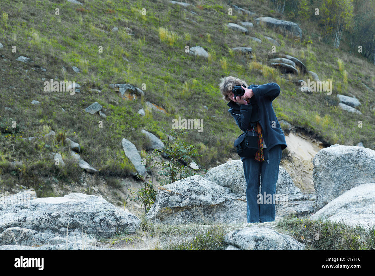 Jolie jolie blondy caucasian heureux succès girl avec l'appareil photo restant dans le paysage de montagne quelqu'un tir. Banque D'Images