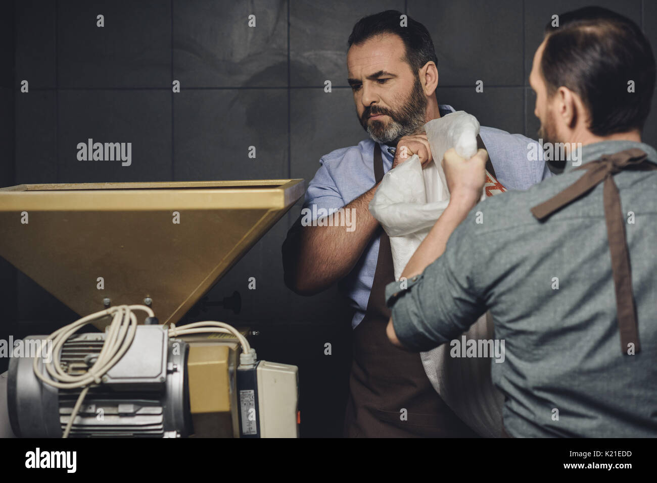 Les hommes en tenue tabliers sac avec grains à la brasserie Banque D'Images