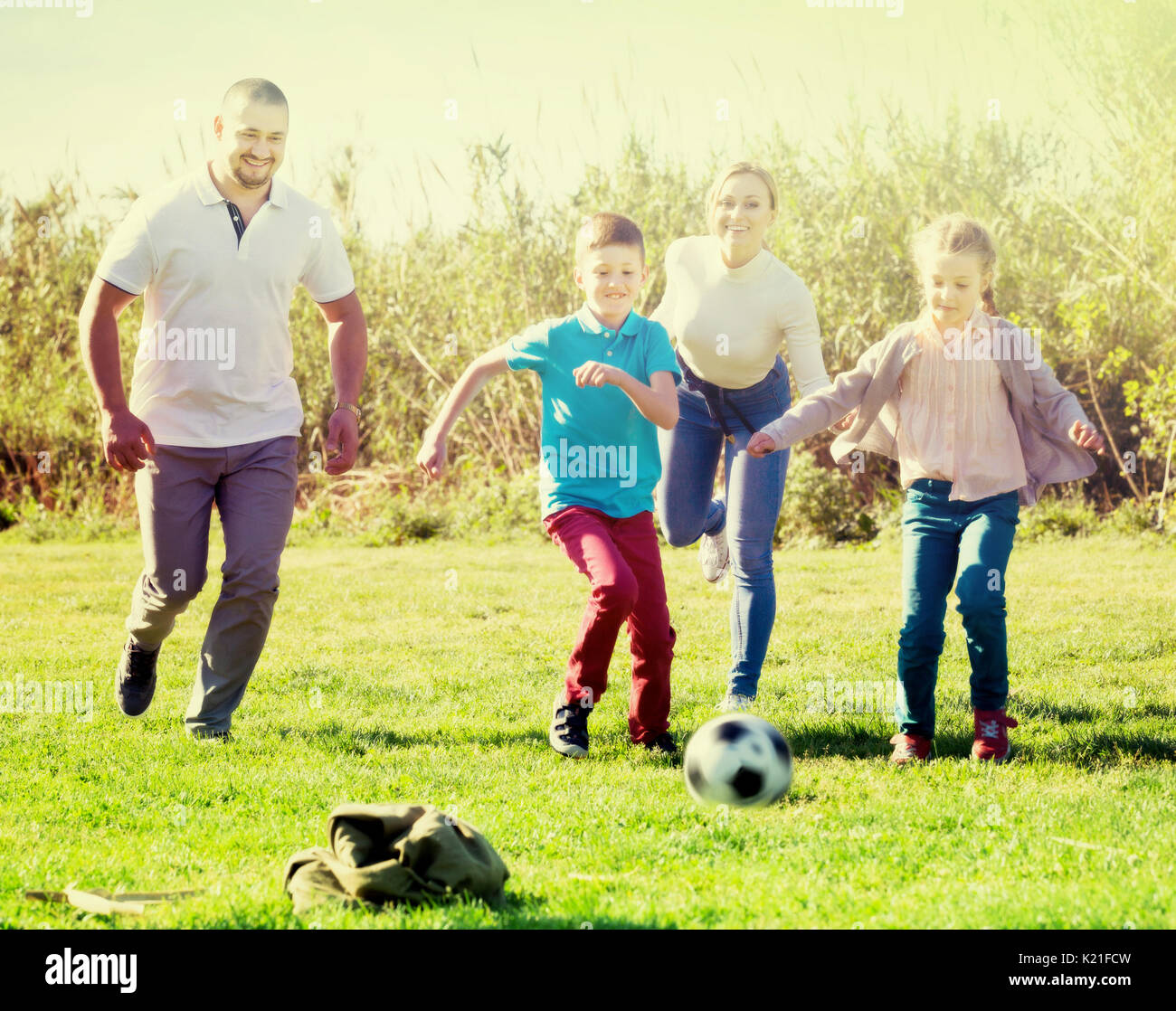 Famille de quatre personnes jouant joyeusement dans le football et rire ensemble à l'extérieur Banque D'Images