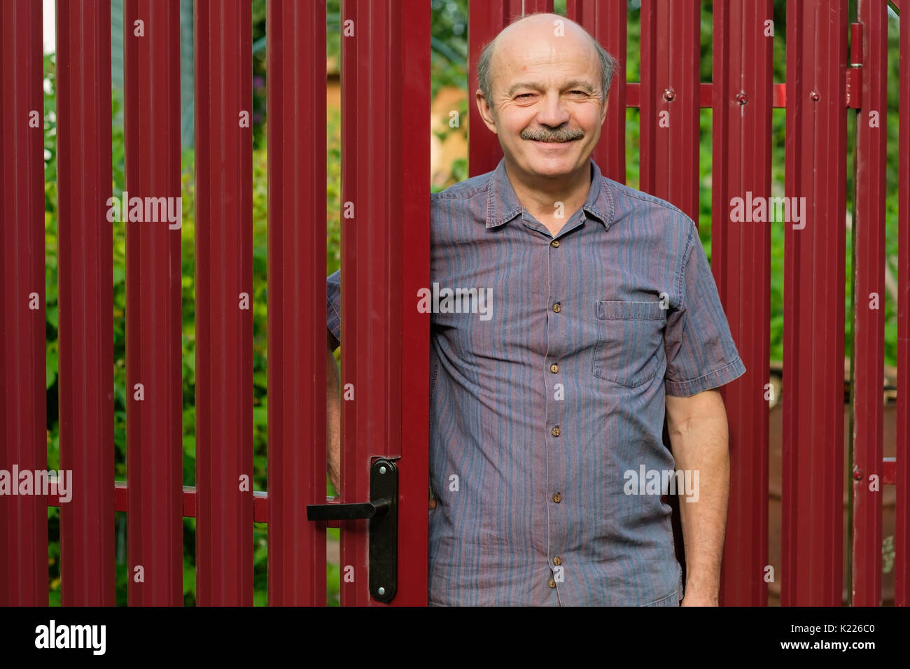 Un homme âgé se réunit des invités lors d'une clôture métallique rouge. Banque D'Images