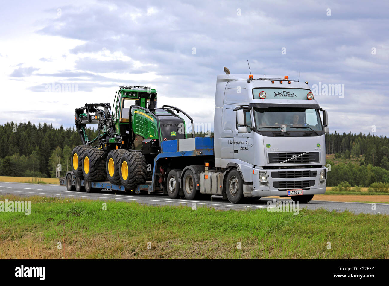 JOKIOINEN, FINLANDE - le 25 août 2017 : Argent Volvo FH12 John Deere 1270G transports forestiers à roues récolteuse sur remorque col de cygne, le long de la route sur un c Banque D'Images