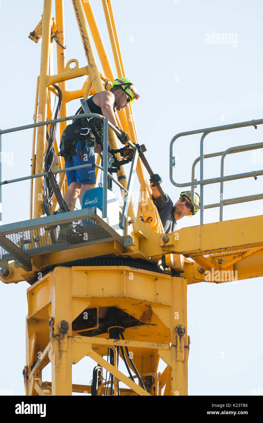 Les travailleurs dans le processus de retrait d'un démontage de grue à tour il bit par bit. Les deux principaux de fixation du bras de flèche sont desserrés à l'aide d'un marteau. Banque D'Images