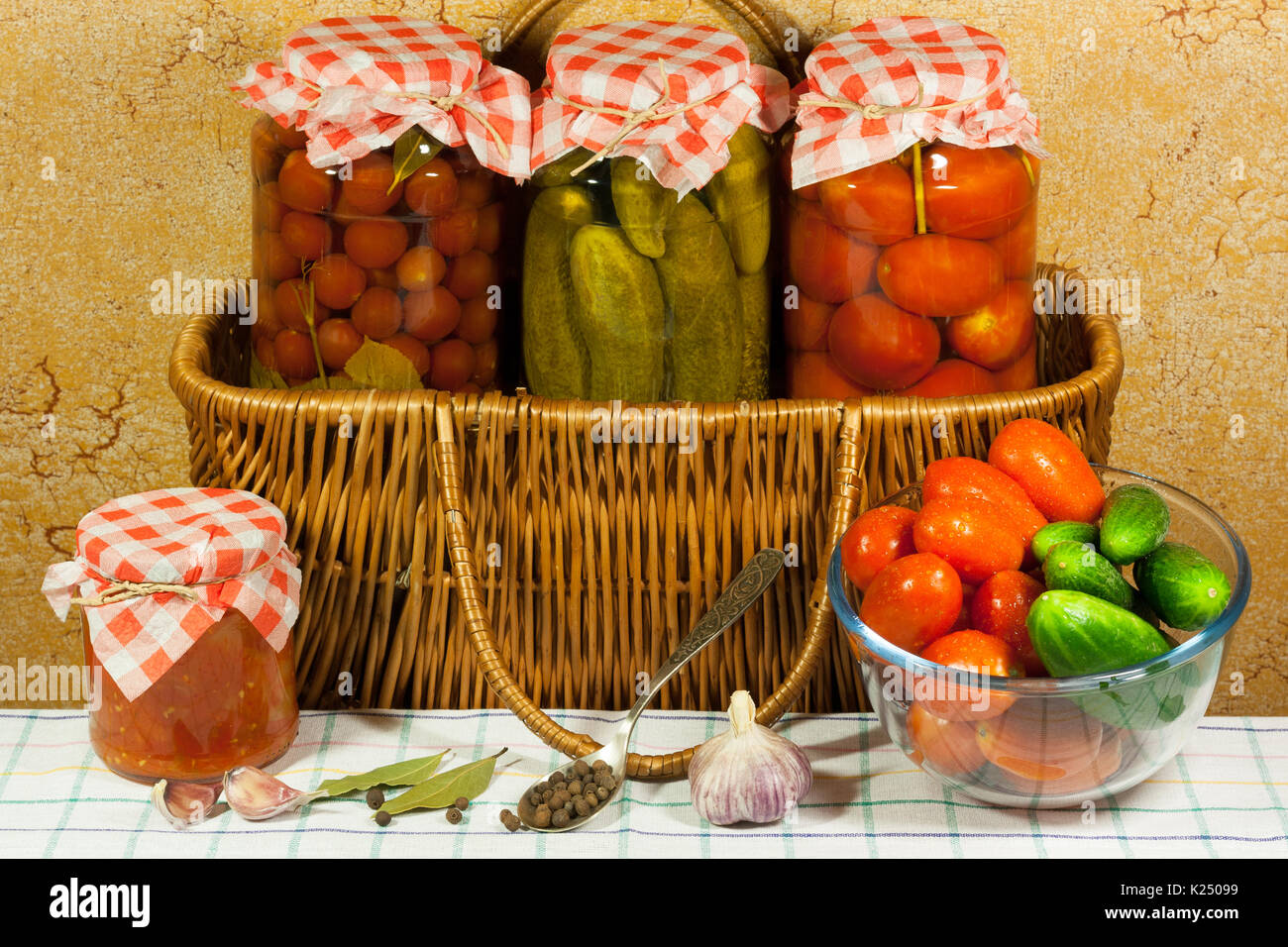 Conserves de légumes (tomates, concombres, tomates cerises) dans un bocal en verre sur panier en osier, des légumes frais (tomates, concombres) dans bol en verre, avec cuillère Banque D'Images