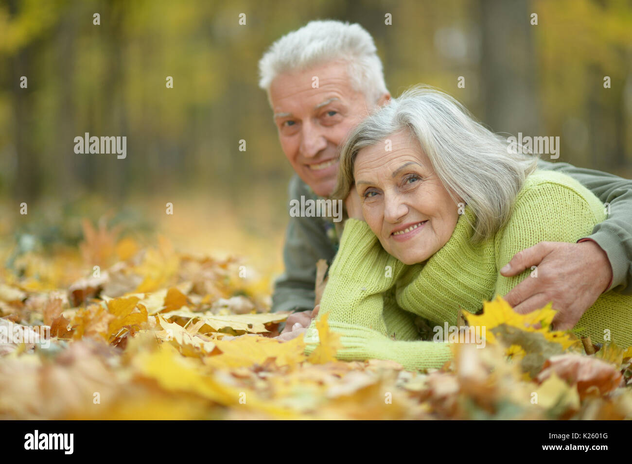 Vieux couple lying on tombé autumnal leaves in park et looking at camera Banque D'Images