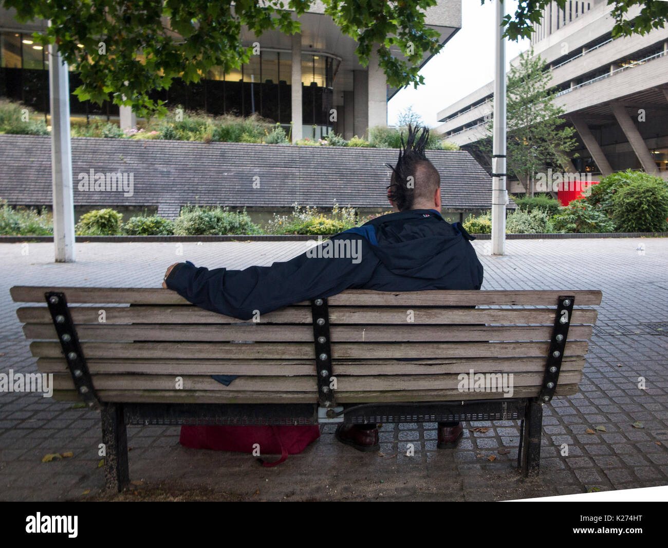 Un homme avec une coupe de mohican détente sur un banc Banque D'Images