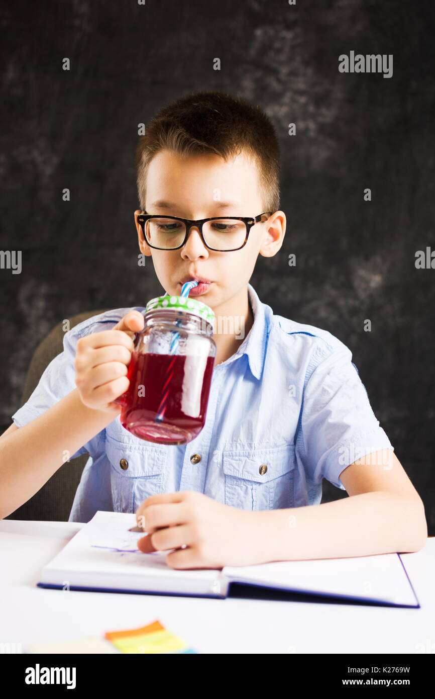 Boy boire du jus tout en terminant ses devoirs à la maison Banque D'Images