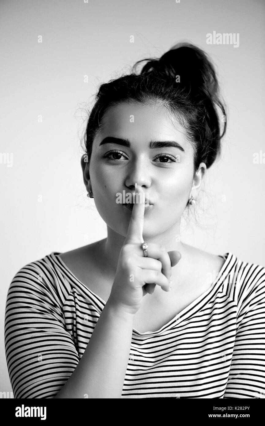 Belle jeune fille aux cheveux noirs et les yeux bruns. Avec la peau rougeoyante propre .les émotions. un doigt à ses lèvres, noir et blanc Banque D'Images