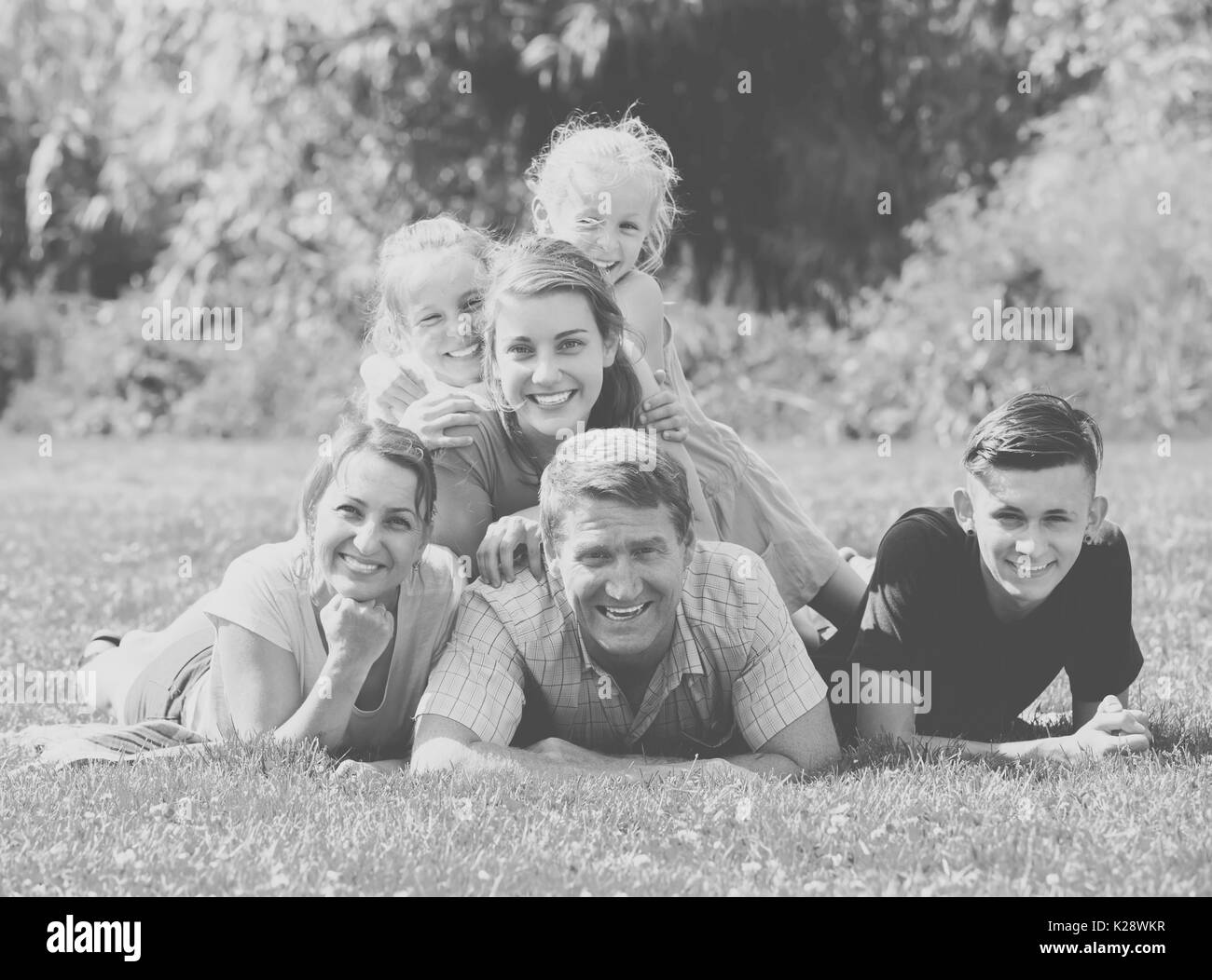 Portrait de grande famille avec les parents et les quatre enfants lying together sur pelouse verte à l'extérieur Banque D'Images